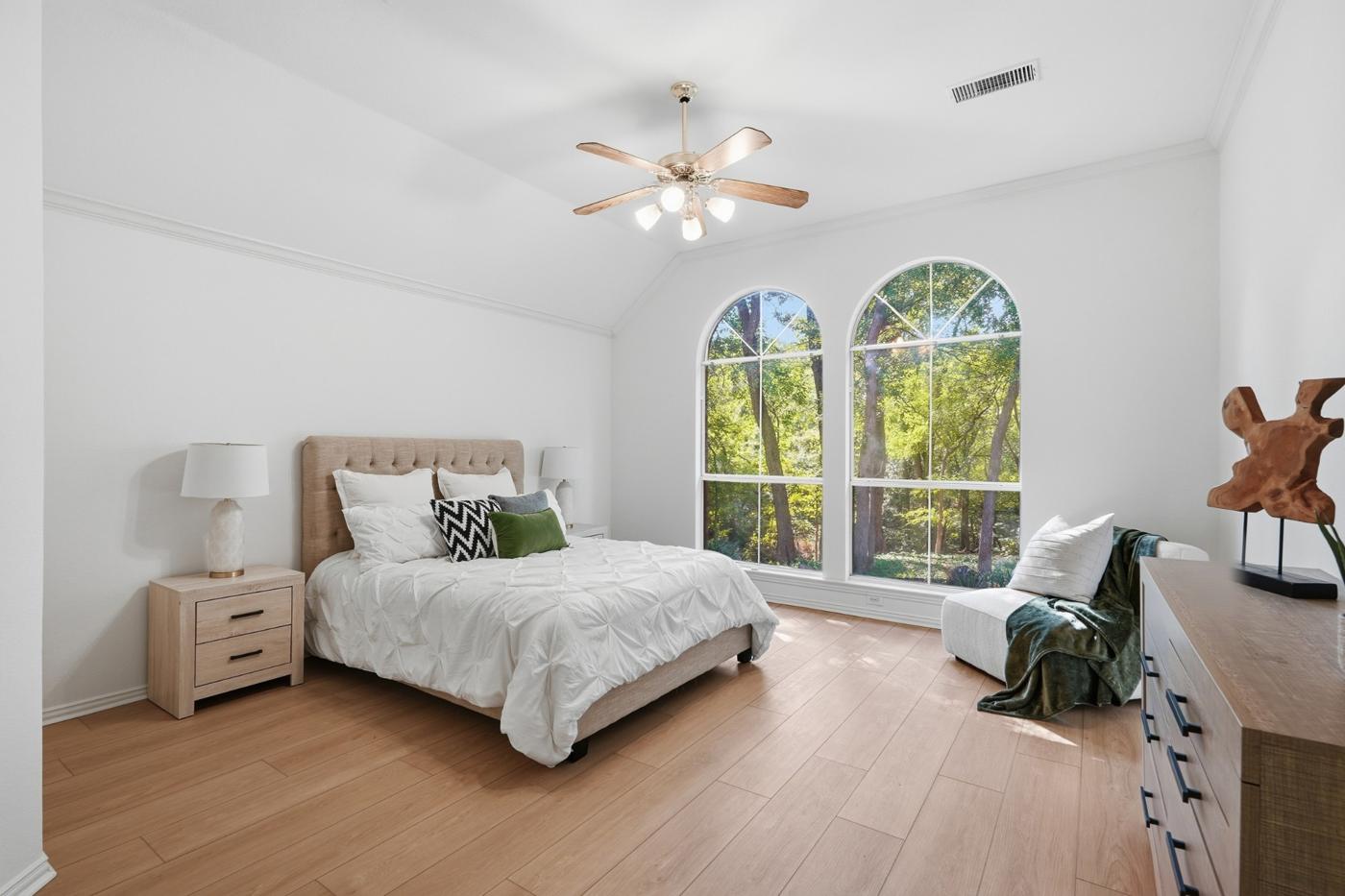 Primary bedroom with vaulted ceiling and two arched windows facing the trees