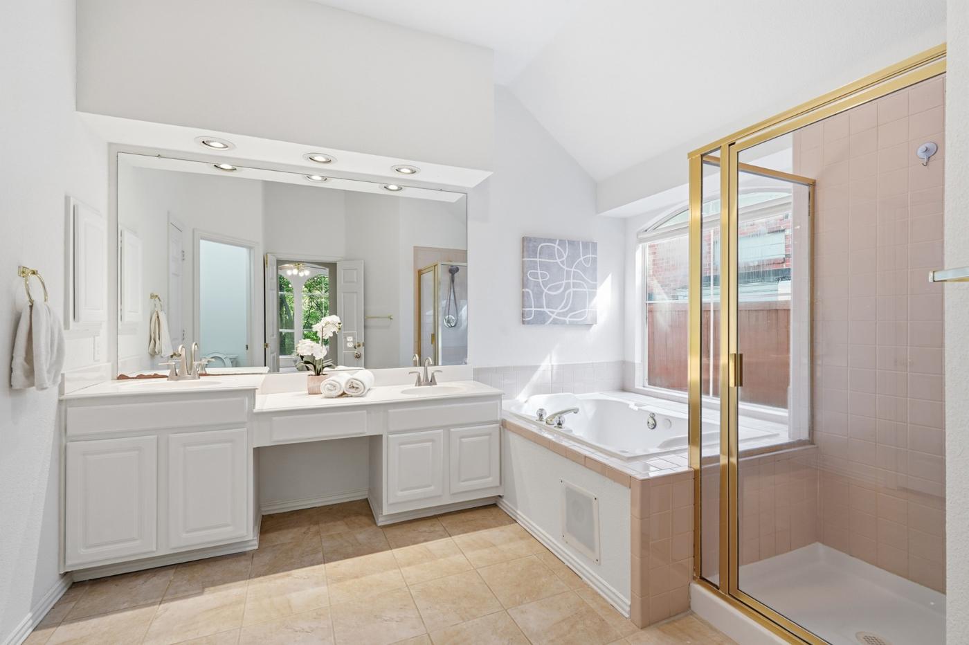 Primary bath with dual sinks, vanity, jetted tub, and separate shower