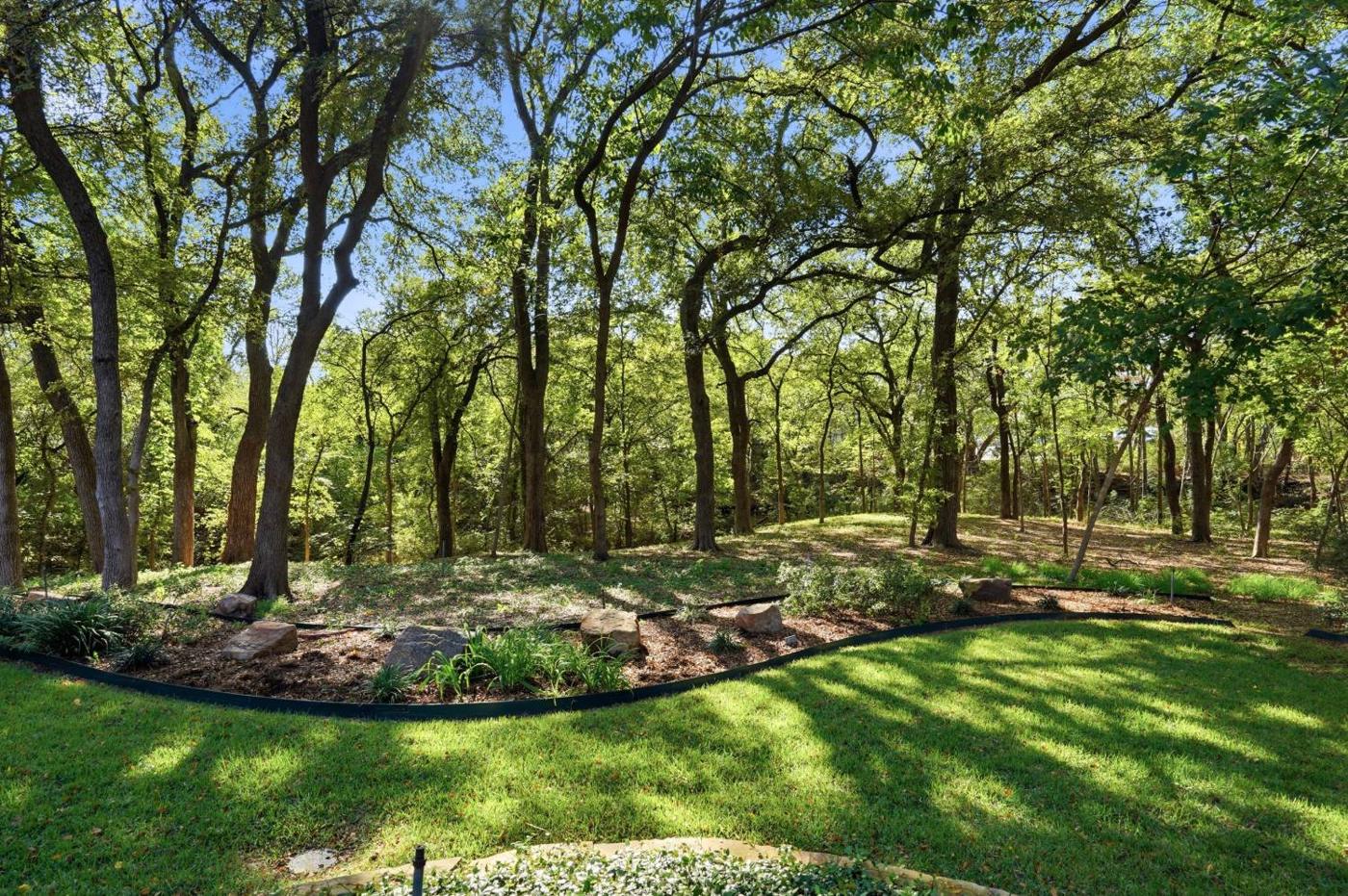 Wooded fenced backyard with mature trees and landscaped beds
